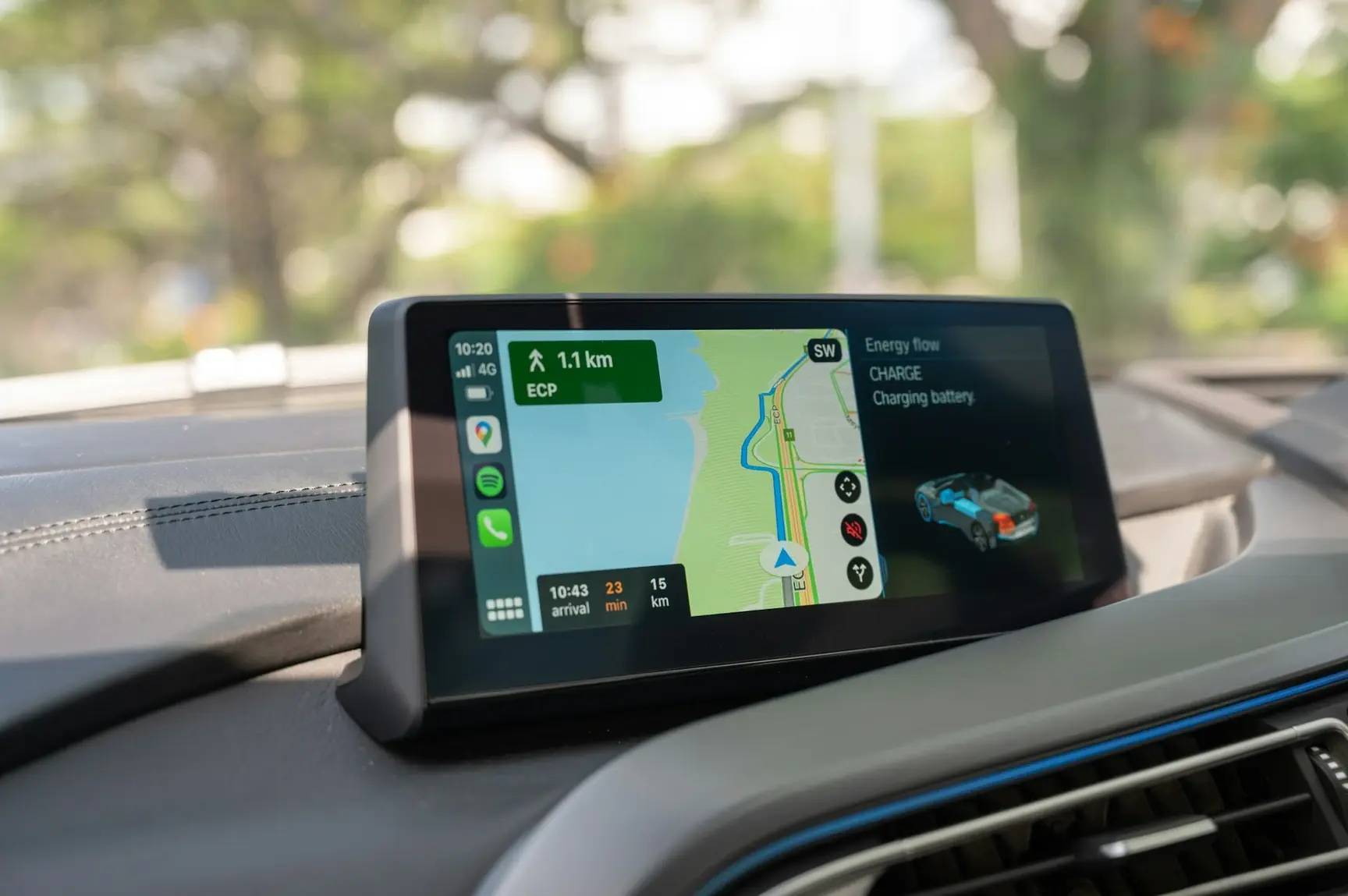 Car dashboard display showing GPS navigation map, route directions, and electric vehicle charging status on a sunny day.