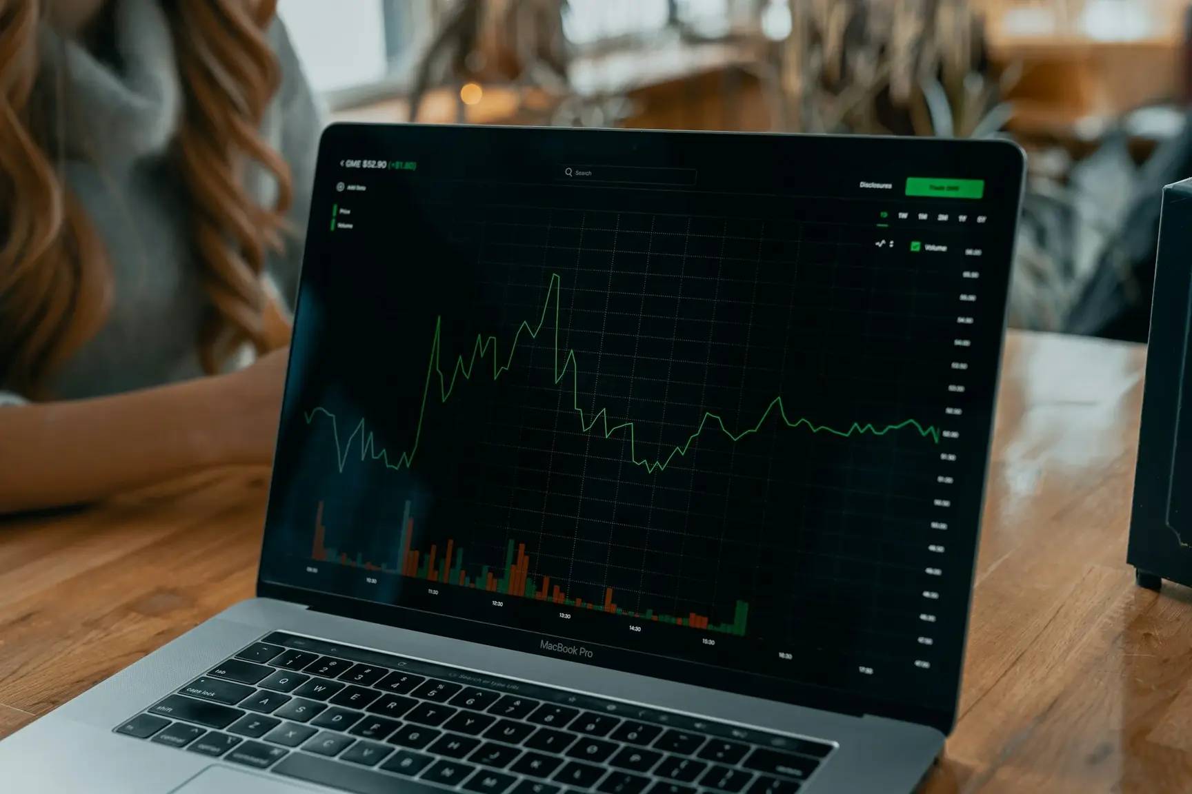 A laptop displaying a financial chart with fluctuating stock prices and volume bars, used for investment tracking and market analysis.